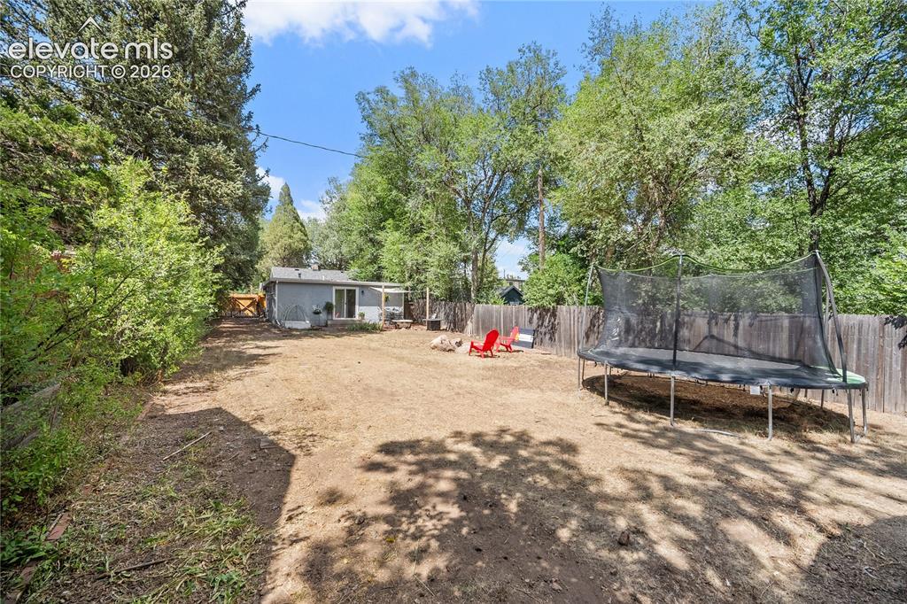 Image 39 of 41: Expansive backyard featuring a privacy fence, mature trees, and a fire pit