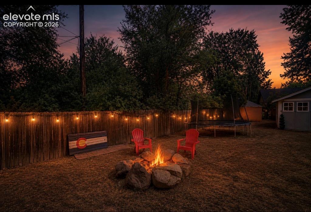 Image 41 of 41: Private backyard featuring a rock fire pit, wood fence, string lighting, an