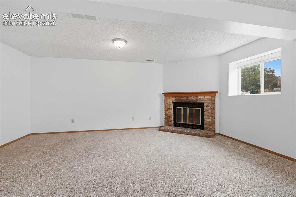 Image 18 of 29: Spacious family room featuring a corner brick fireplace with a wood mantle,