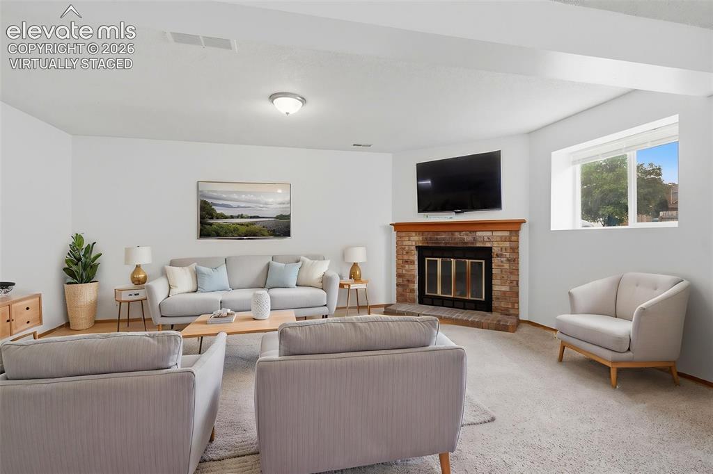 Image 19 of 29: Spacious living area featuring a brick fireplace with a wood mantle, carpet