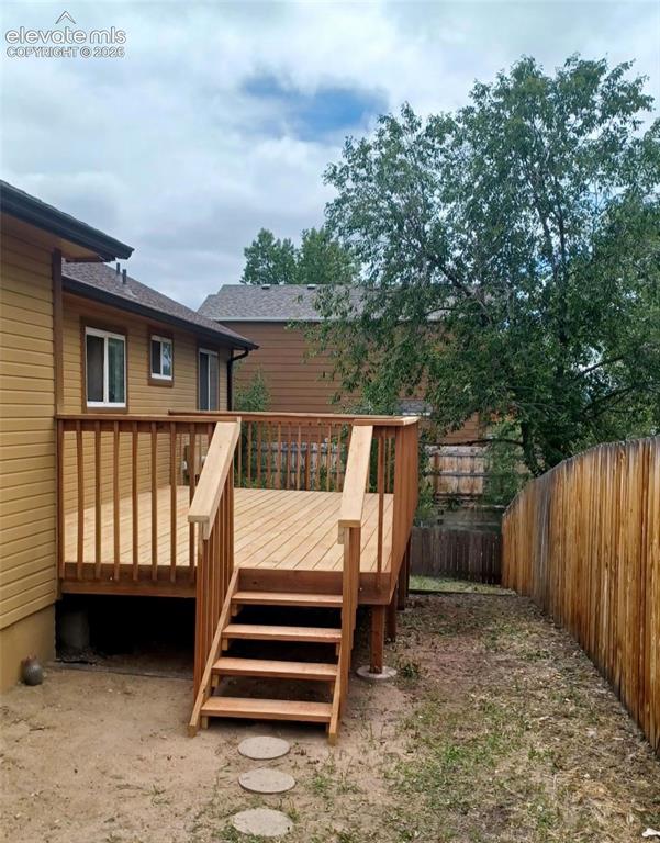 Image 27 of 29: Wooden deck with railing and stairs, set against a house with light brown s