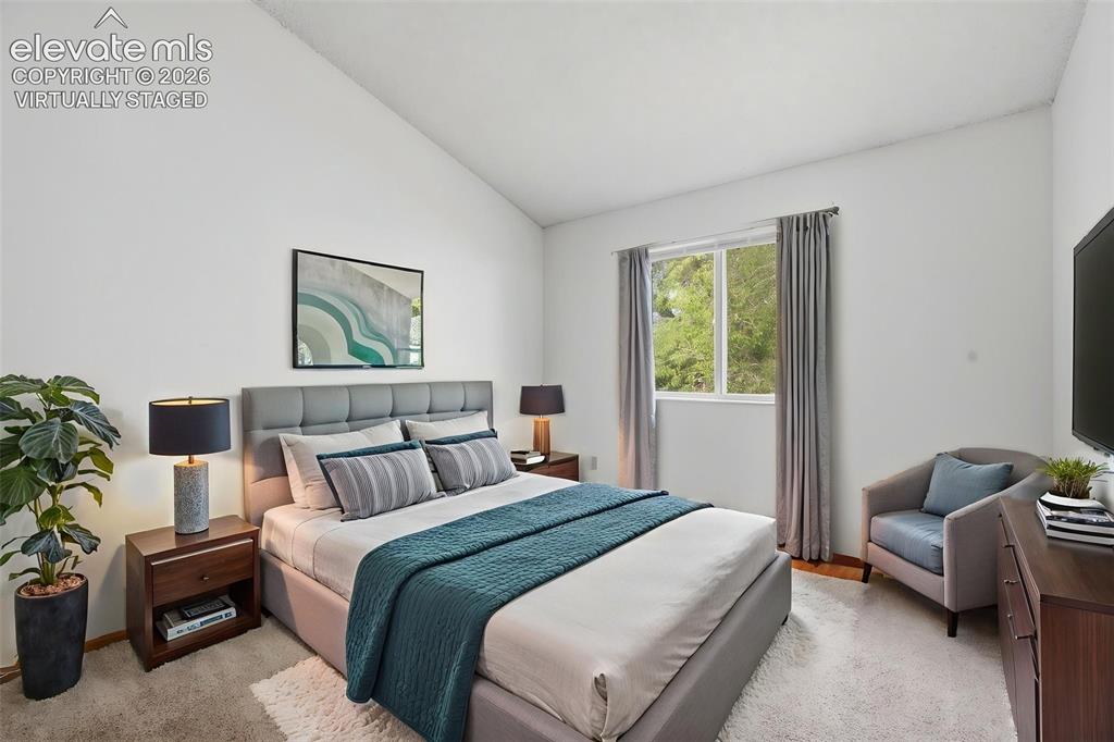 Image 9 of 29: Vaulted ceiling bedroom with a large window, plush carpet, and two dark woo