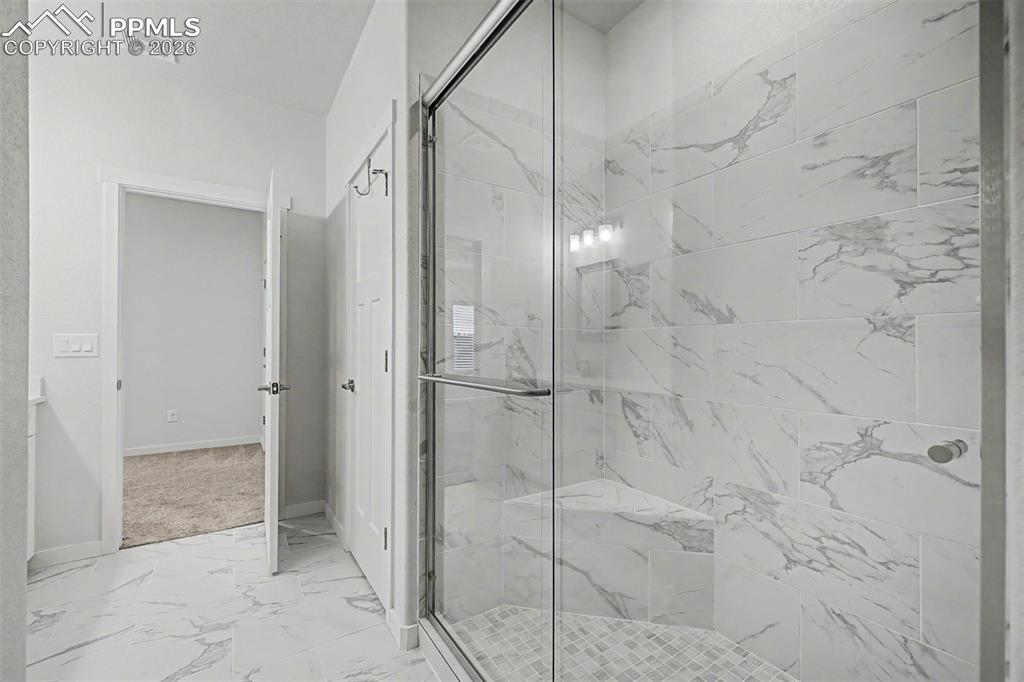 Image 23 of 39: A floor-to-ceiling marble-look tile walk-in shower with a built-in bench an