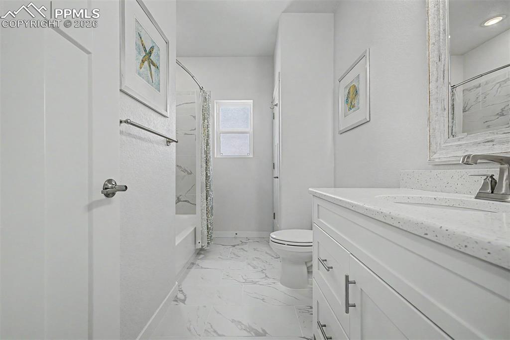 Image 29 of 39: The shared hall bath is bright and polished, with marble-look tile floors,