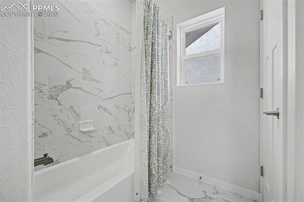 Image 30 of 39: The tub and shower combo is finished in dramatic marble-look tile, with a d