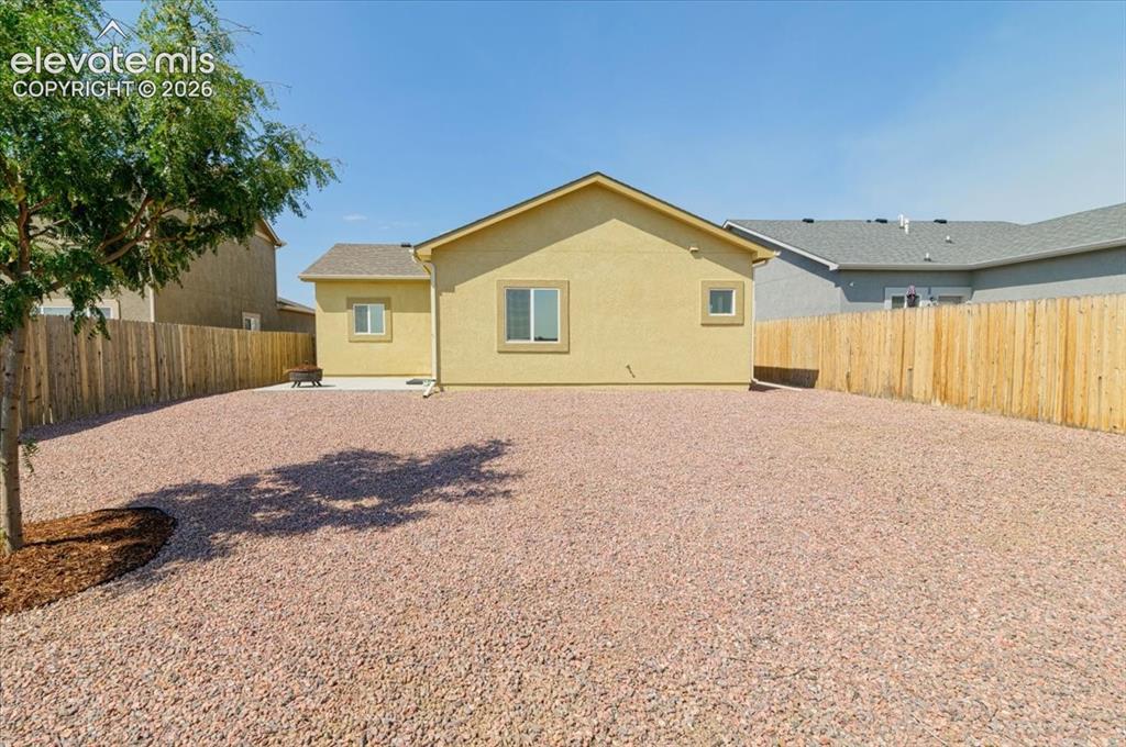 Image 22 of 36: Expansive gravel yard with wood privacy fencing, a mature tree, and a stucc