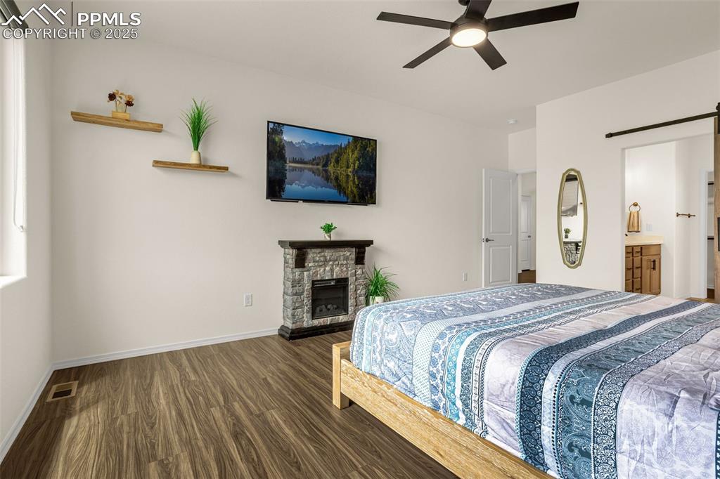 Image 17 of 41: Bedroom with dark wood finished floors, a barn door, a fireplace, ceiling f