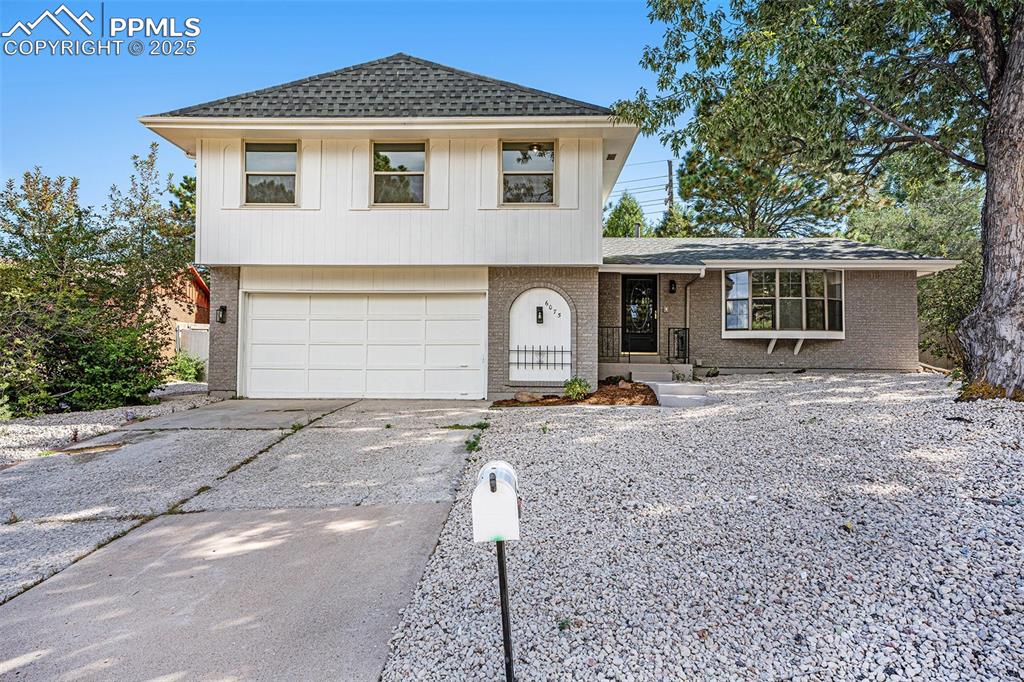 Caption: View of front of home featuring roof with shingles, driveway, brick siding, and a garage