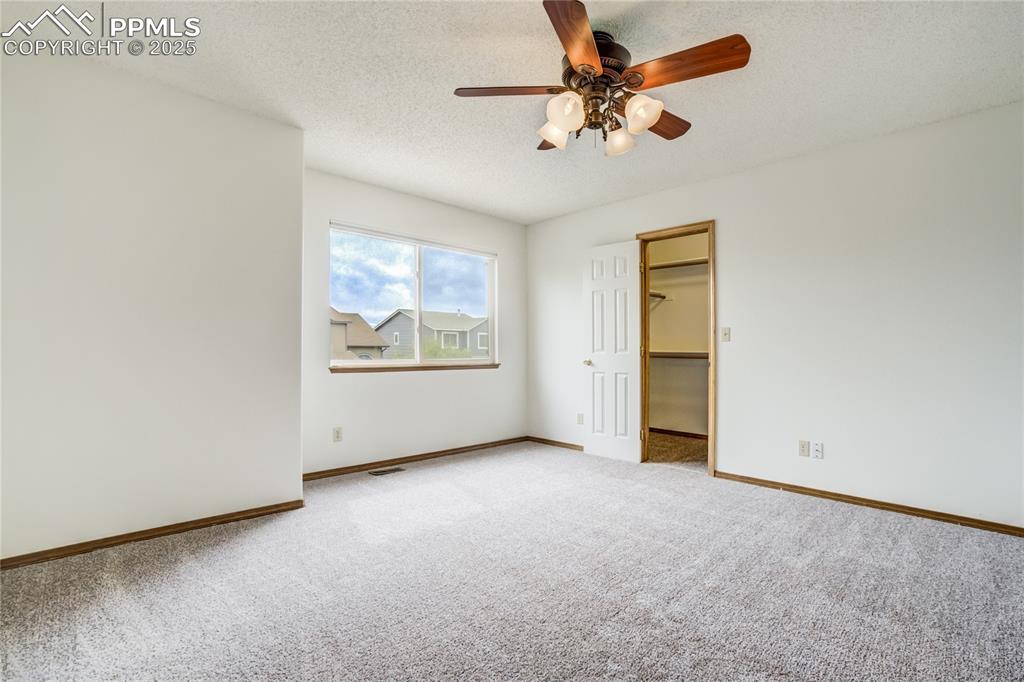 Image 13 of 34: Unfurnished bedroom with a walk in closet, carpet floors, a ceiling fan, an