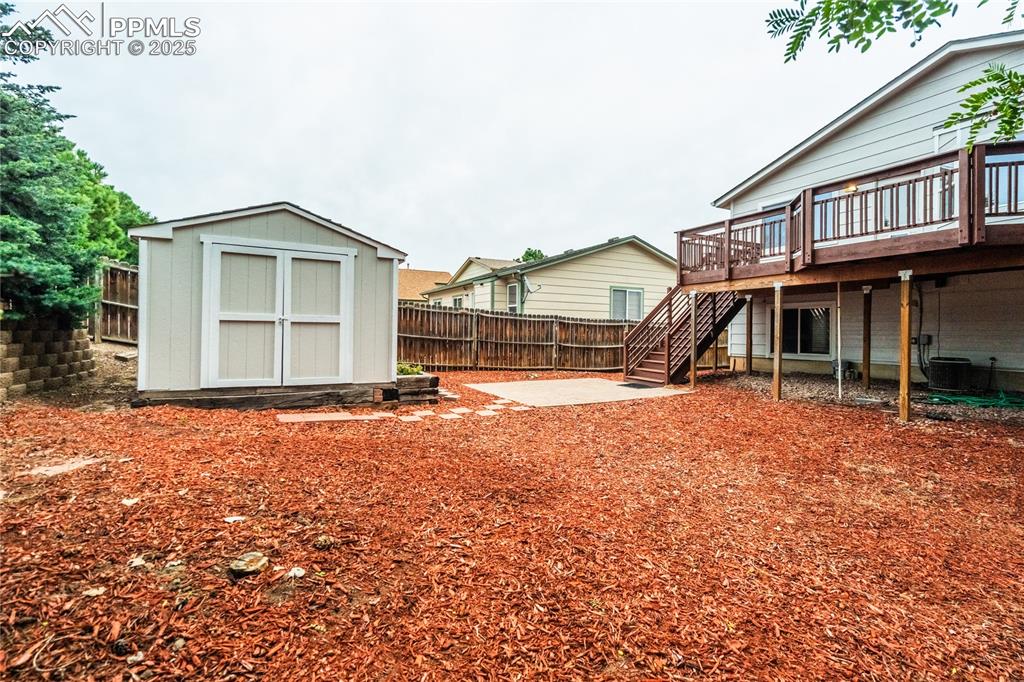 Image 28 of 34: Fenced backyard featuring a wooden deck, a shed, stairway, and a patio area