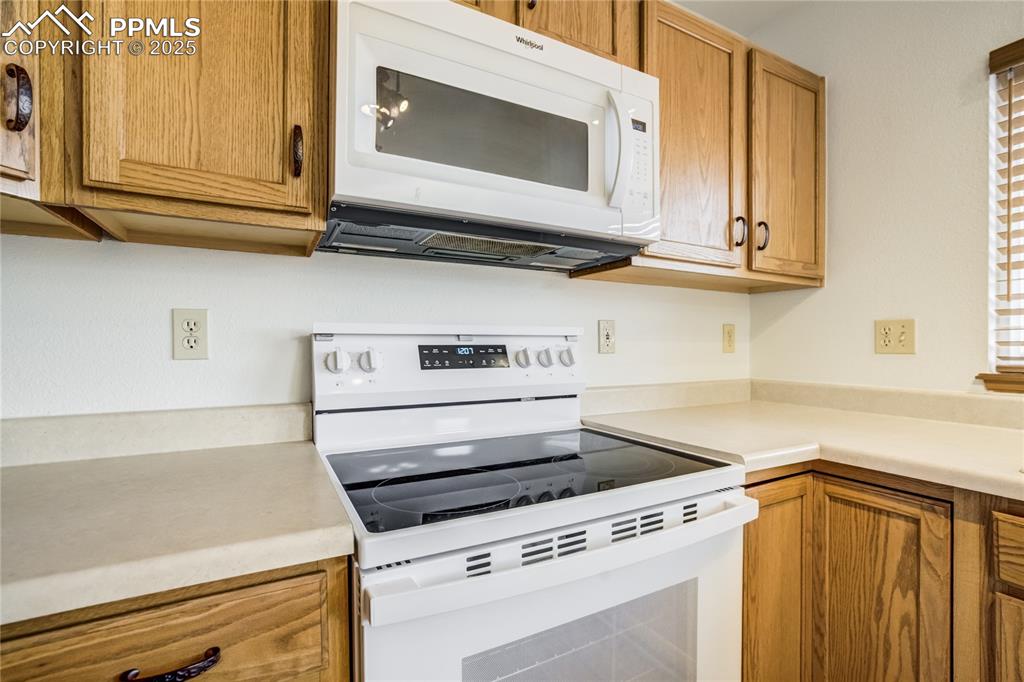 Image 6 of 34: Kitchen with white appliances, brown cabinets, and light countertops