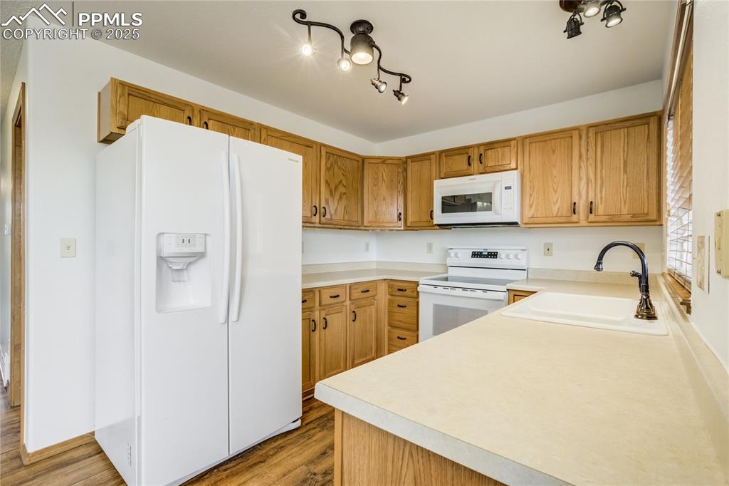 Image 7 of 34: Kitchen featuring white appliances, brown cabinetry, light countertops, and