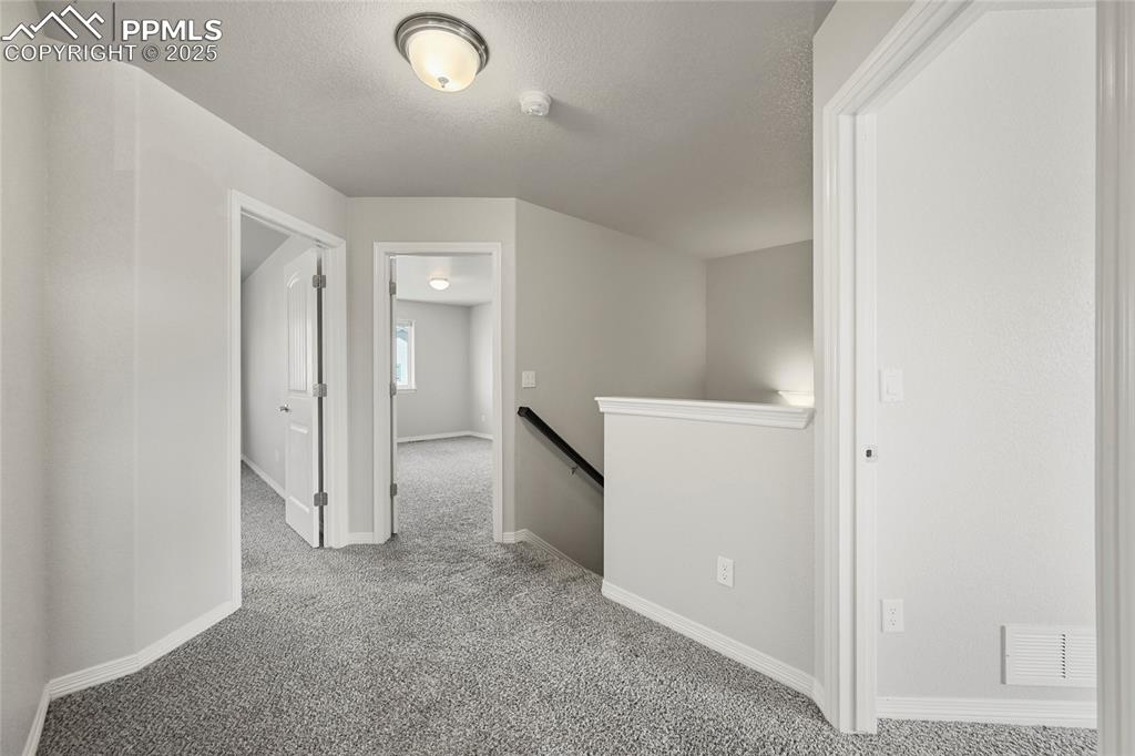 Image 14 of 29: Hallway with an upstairs landing, carpet floors, and a textured ceiling