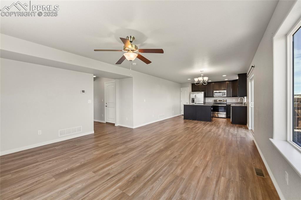 Image 8 of 29: Unfurnished living room with a chandelier, ceiling fan, and wood finished f