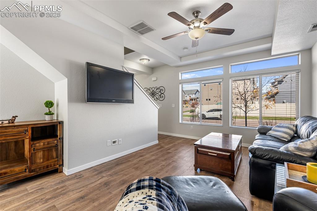 Image 11 of 50: Living room with wood finished floors, a ceiling fan, and a raised ceiling