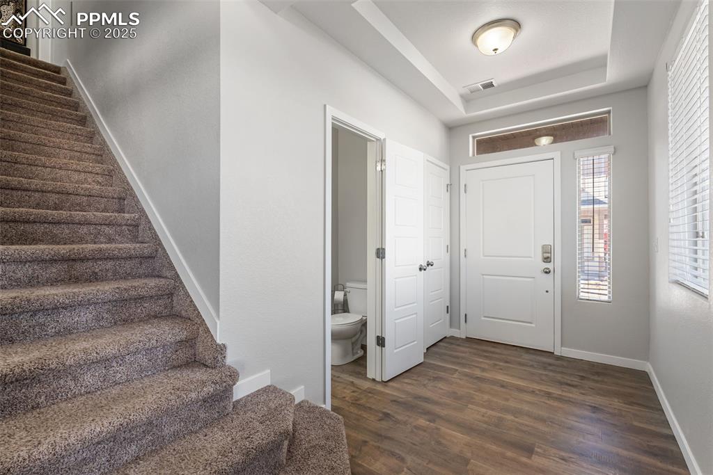 Image 14 of 50: Entrance foyer with a raised ceiling, stairway, and dark wood-style floors