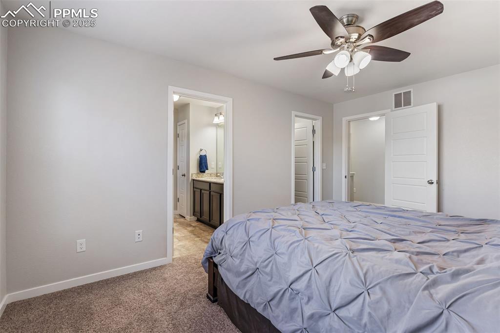 Image 18 of 50: Bedroom with light carpet, ceiling fan, and connected bathroom