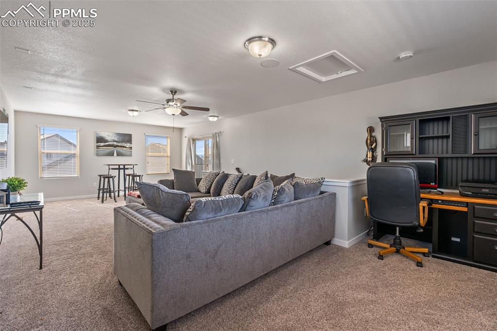 Image 33 of 50: Living room with carpet floors, a desk, attic access, and a ceiling fan