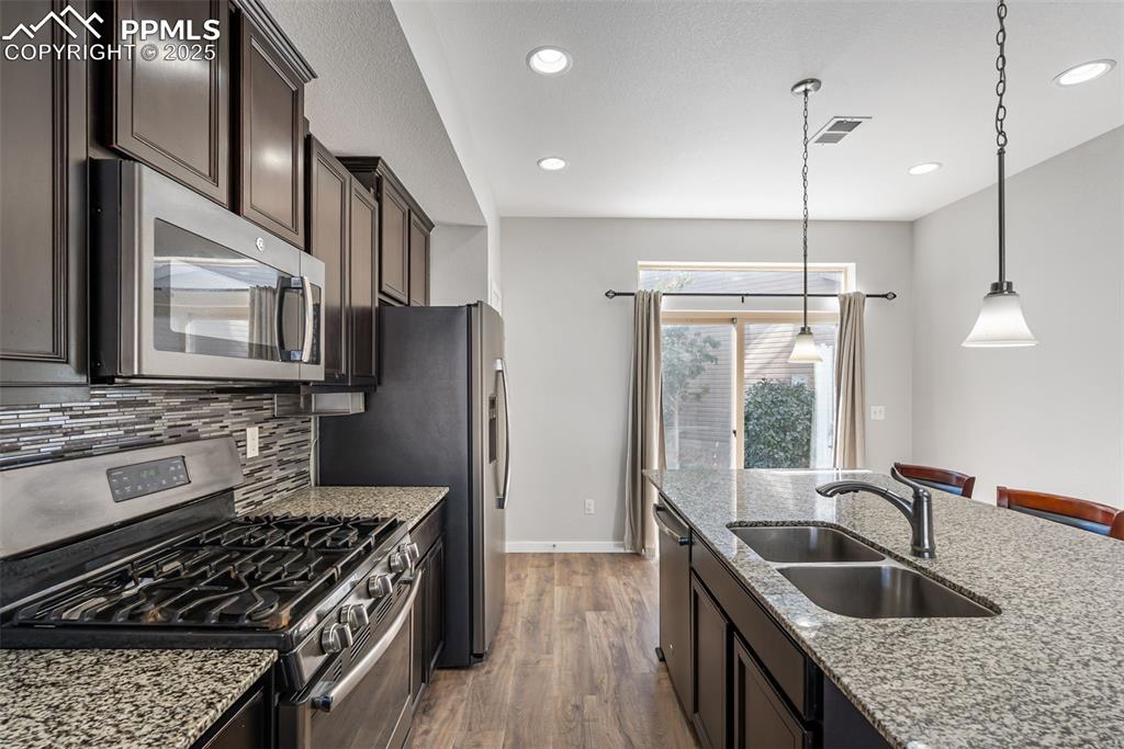 Image 6 of 50: Kitchen with stainless steel appliances, dark brown cabinets, light stone c