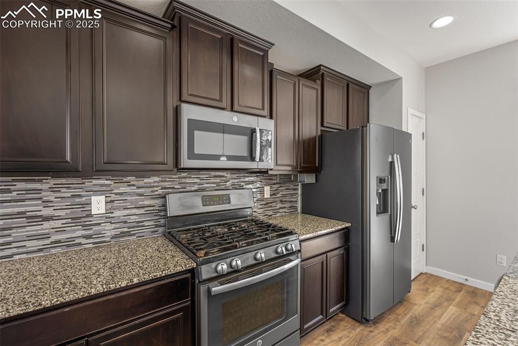 Image 7 of 50: Kitchen featuring stainless steel appliances, dark brown cabinets, light wo
