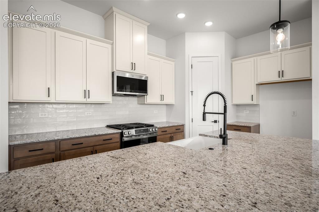 Image 12 of 45: Spacious island featuring a white farmhouse sink with a matte black pull-do