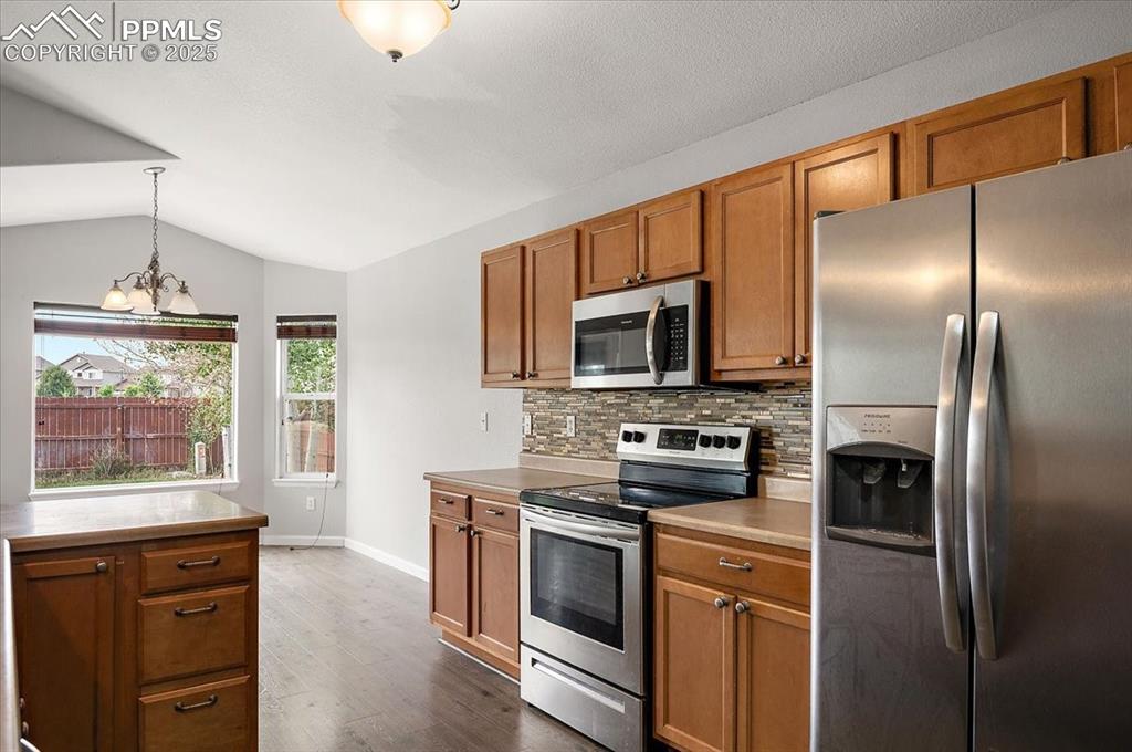 Image 10 of 35: Kitchen with appliances with stainless steel finishes, brown cabinetry, lof