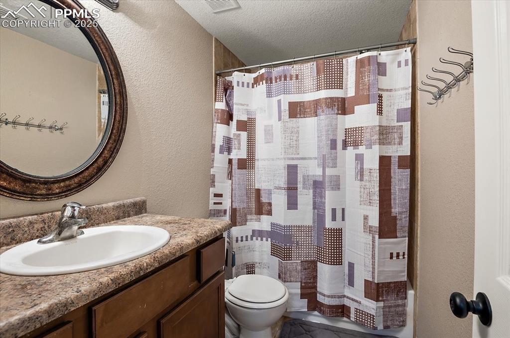 Image 15 of 35: Full bath featuring a textured wall, a textured ceiling, vanity, and curtai