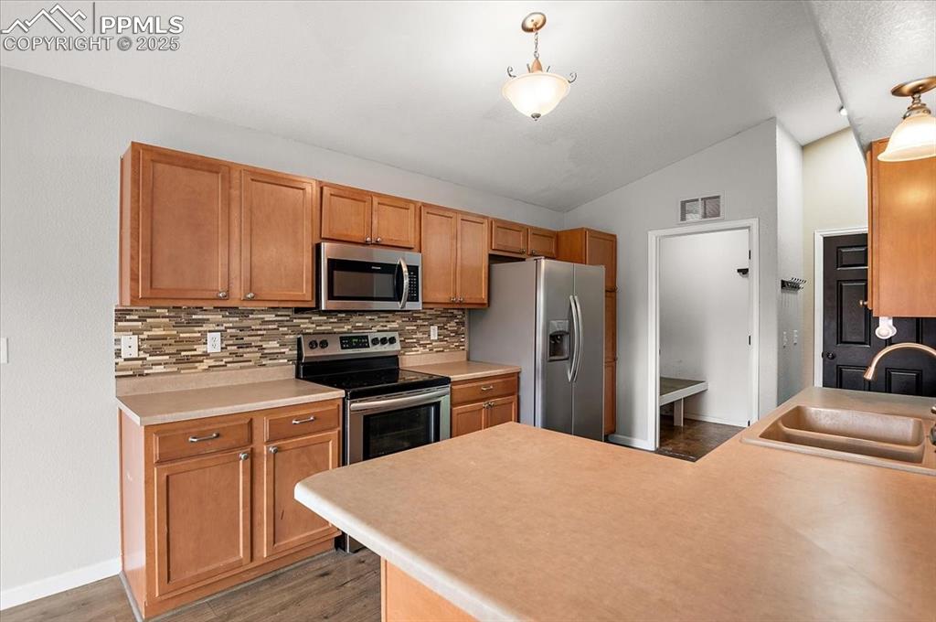 Image 9 of 35: Kitchen with lofted ceiling, decorative backsplash, appliances with stainle