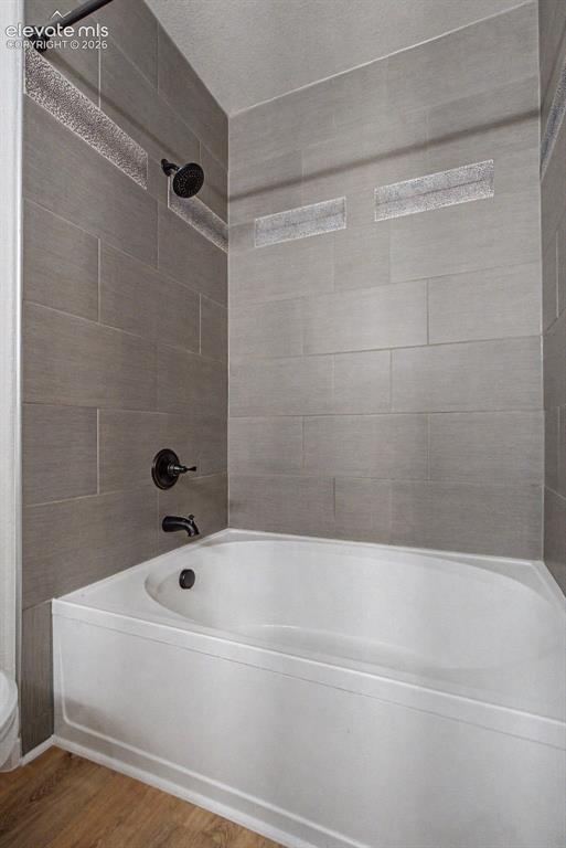 Image 21 of 23: Bathtub and shower combination featuring large format grey wall tiles with 