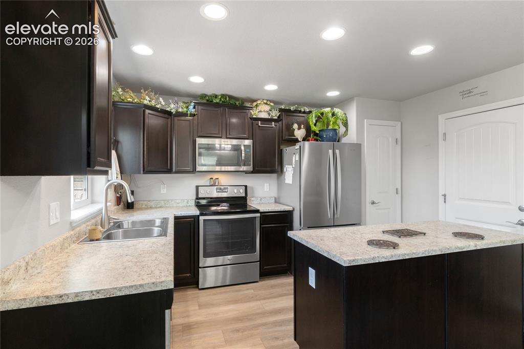 Image 14 of 38: Dark wood-finish cabinetry with stainless steel appliances, light-toned cou