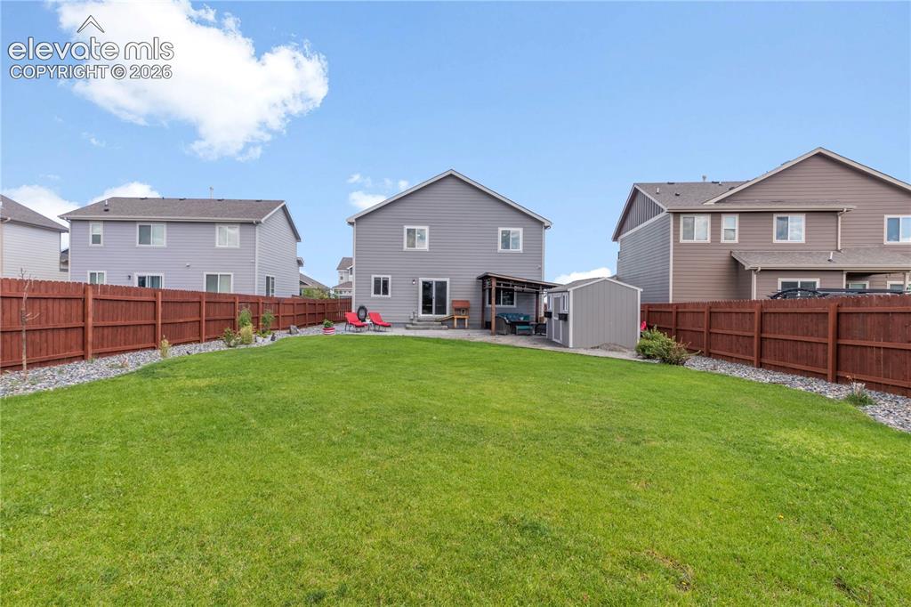 Image 36 of 38: Expansive backyard with a manicured lawn, wood privacy fencing, and a grave
