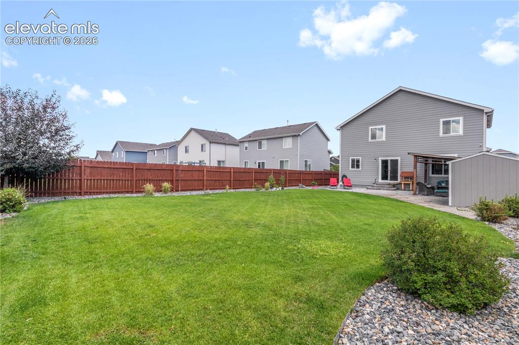 Image 37 of 38: Expansive green lawn with a brown privacy fence, complemented by a patio ar