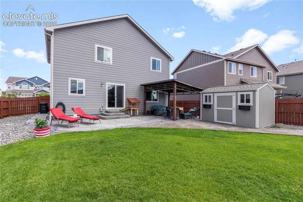 Image 38 of 38: Expansive fenced backyard featuring a manicured lawn, concrete patio, cover