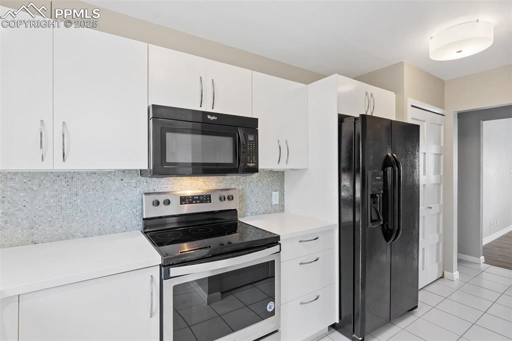 Image 14 of 48: Kitchen featuring black appliances, light countertops, white cabinetry, dec