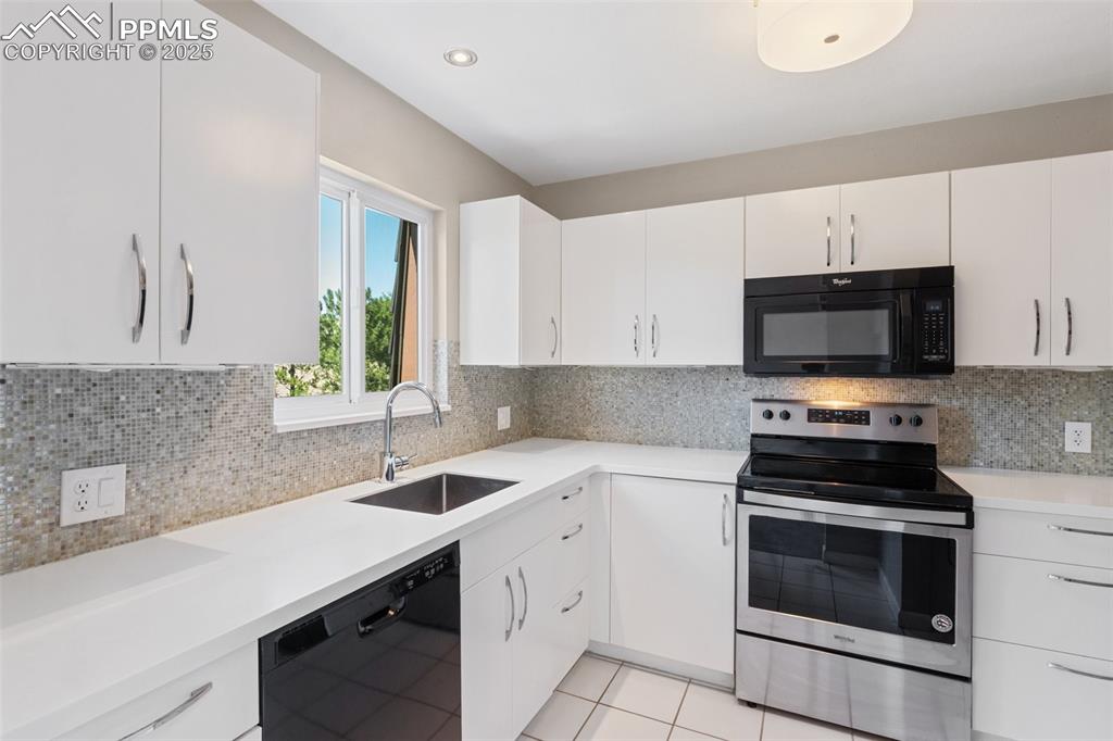 Image 15 of 48: Kitchen with black appliances, light countertops, white cabinetry, decorati