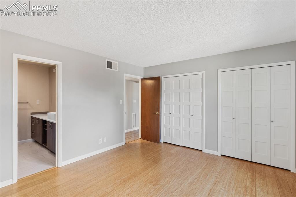 Image 24 of 48: Master Bed featuring two closets, light wood-style flooring, a textured cei