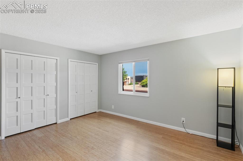 Image 25 of 48: Master Bed with two closets, light wood-style floors, and a textured ceilin