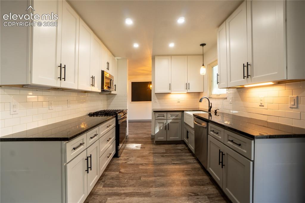 Image 11 of 33: Galley kitchen featuring white upper cabinetry, gray lower cabinetry, black