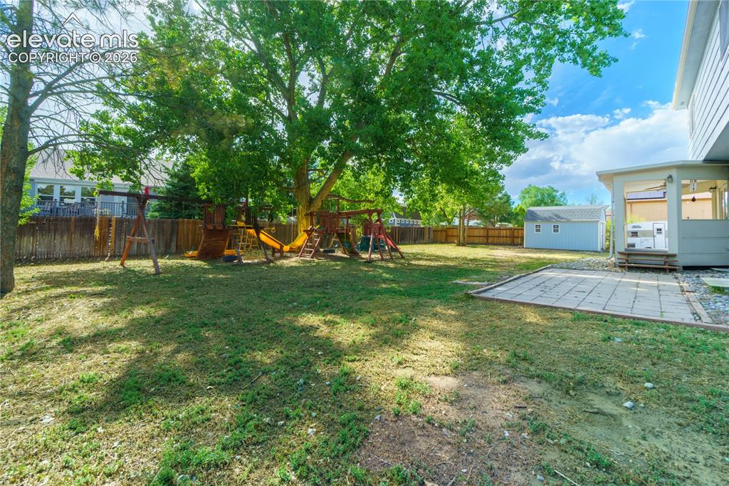Image 32 of 33: Expansive green space featuring mature trees, a paved patio, covered porch,