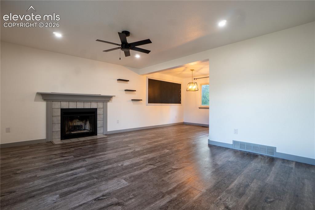 Image 6 of 33: Living area featuring wood-finish flooring, a fireplace with a tiled surrou