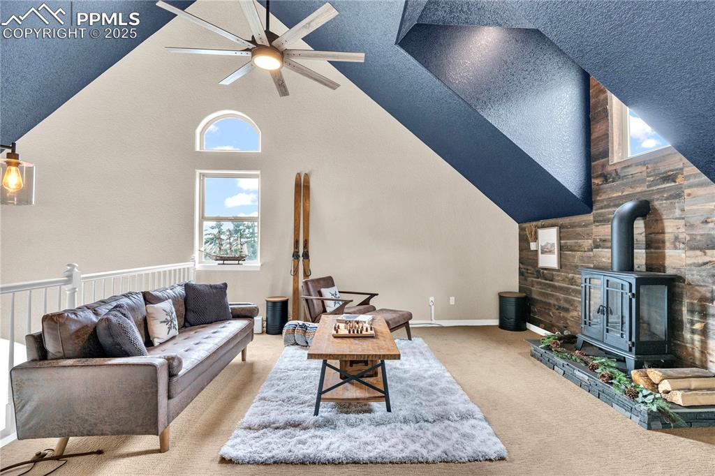 Image 10 of 29: Carpeted living room featuring a wood stove, high vaulted ceiling, ceiling 