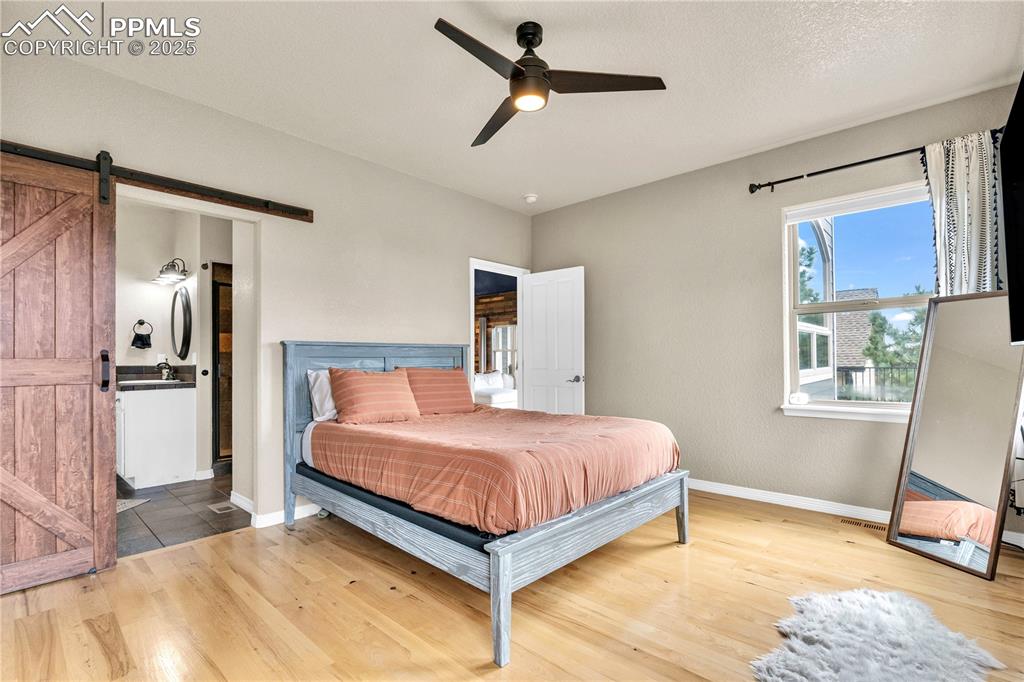 Image 11 of 29: Bedroom with a barn door, wood finished floors, a ceiling fan, and a textur