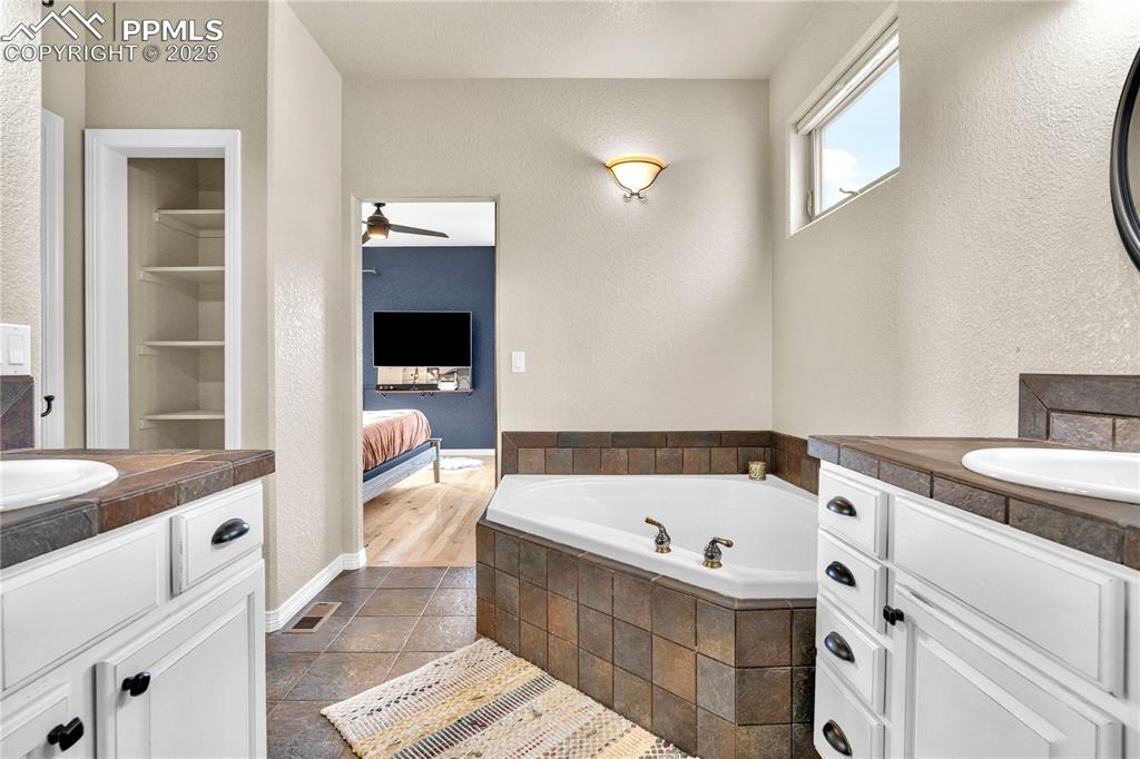 Image 12 of 29: Bathroom with two vanities, a garden tub, a textured wall, a ceiling fan, a