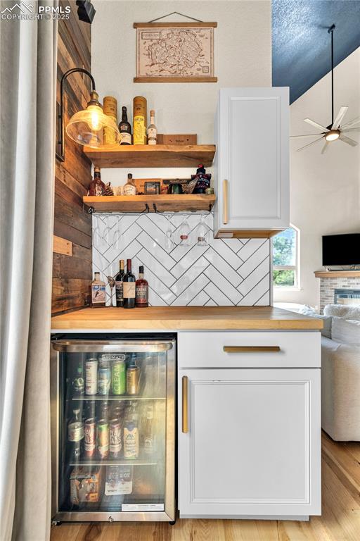 Image 9 of 29: Indoor dry bar featuring beverage cooler, a fireplace, ceiling fan, backspl