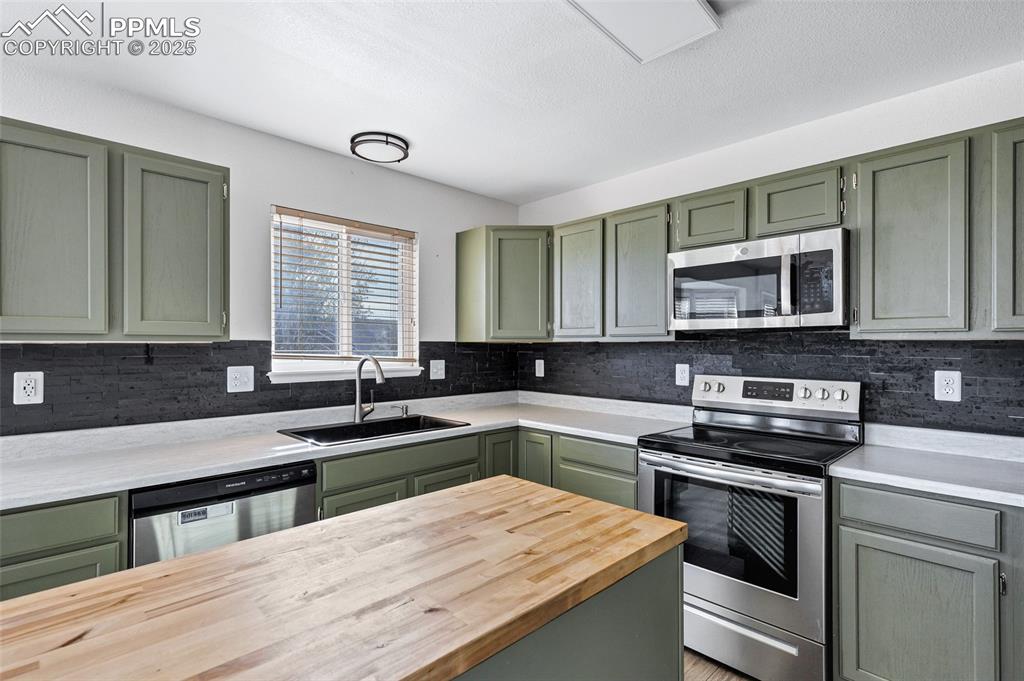 Image 11 of 25: Kitchen featuring green cabinetry, appliances with stainless steel finishes