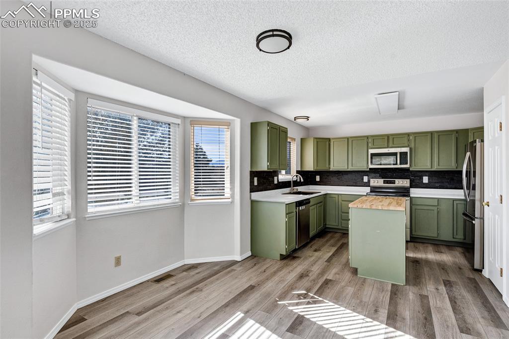 Image 8 of 25: Kitchen with green cabinetry, a textured ceiling, decorative backsplash, an