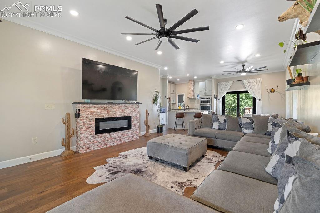 Image 9 of 50: Living area with wood finished floors, ornamental molding, ceiling fan, a f