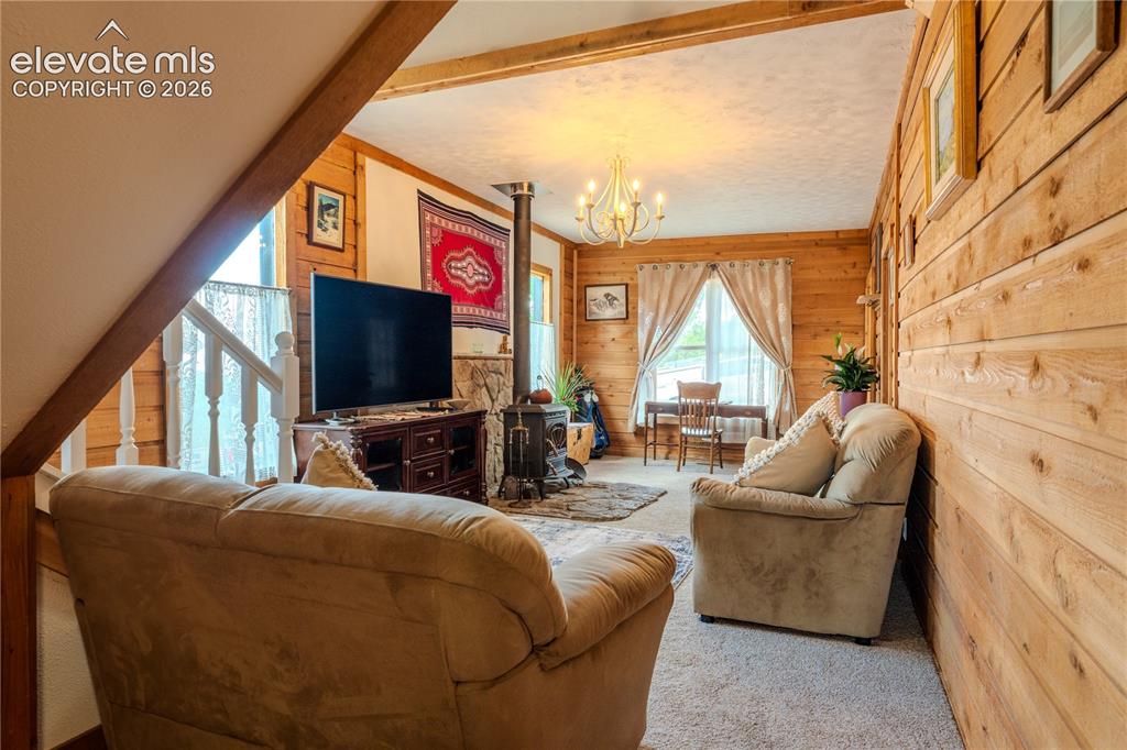 Image 11 of 40: Wood-paneled interior walls featuring exposed wood beams and a stone firepl