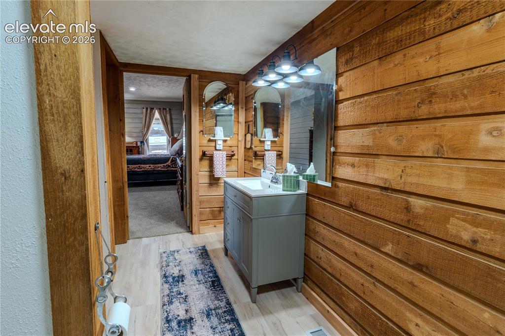 Image 20 of 40: Wood-paneled bathroom with a single vanity, rectangular mirror, and sconce