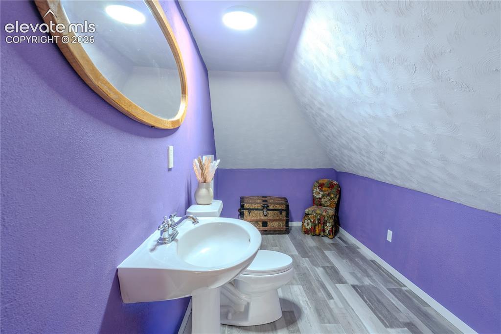Image 28 of 40: Bathroom featuring a wall-mounted sink, pedestal toilet, wood-finish floori